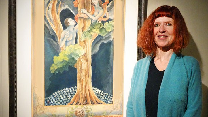 Photo of Rita O'Hara an artist living with Rheumatoid Arthritis. She stands next to her art of Adam and Eve in a tree with a snake.