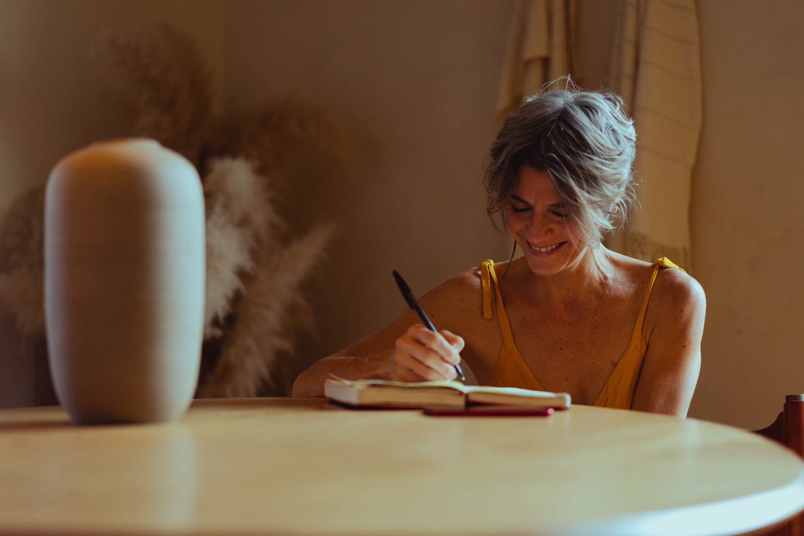 A woman smiles as she writes in her gratitude journal, a good practice for chronic illness acceptance.
